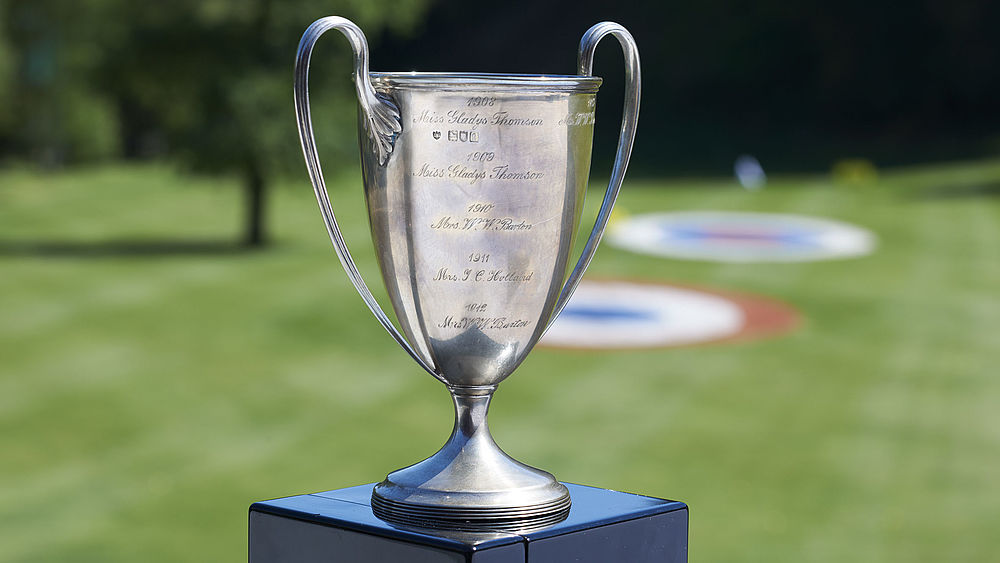 Silver trophy with curved handles on a plinth against the backdrop of the green golf course. Bright and sunny, evoking a sense of victory and achievement.