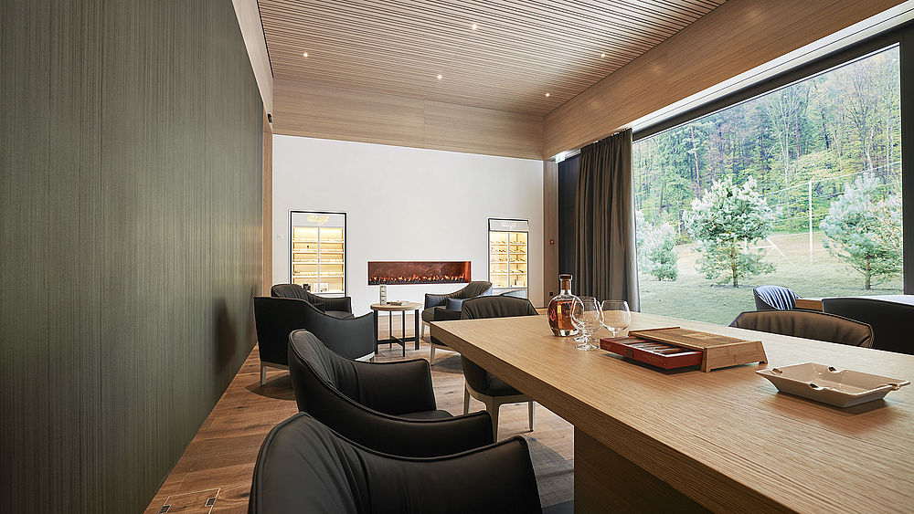 he Smokers Lounge in the clubhouse is a modern room with a long wooden table, black chairs and a decorative ceiling. A large window overlooks the driving range, creating a tranquil atmosphere.