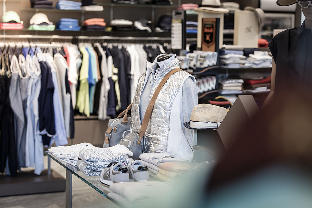Golfbekleidungsgeschäft mit übersichtlichen Auslagen. Hemden und Jacken hängen in Regalen, gefaltete Artikel in Regalfächern und schaffen eine aufgeräumte und einladende Einkaufsatmosphäre.