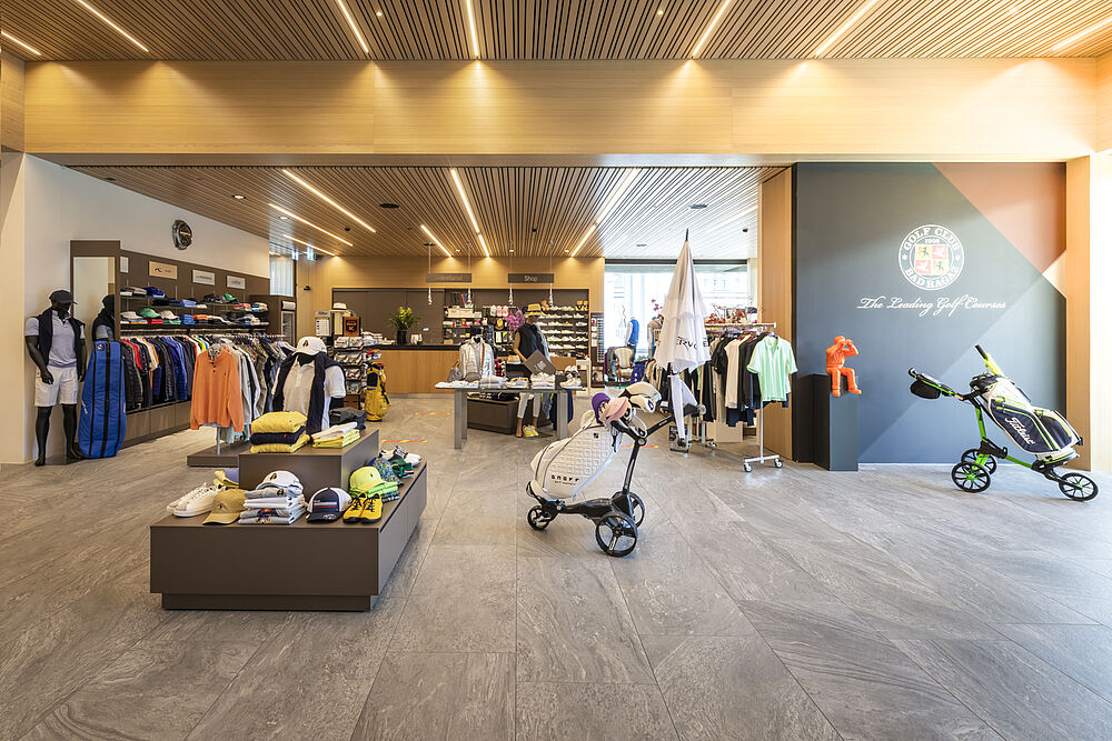 Modernes Golfgeschäft mit Bekleidungsauslagen, Golfausrüstung und Zubehör bei warmer Beleuchtung. Die Atmosphäre ist elegant und einladend.