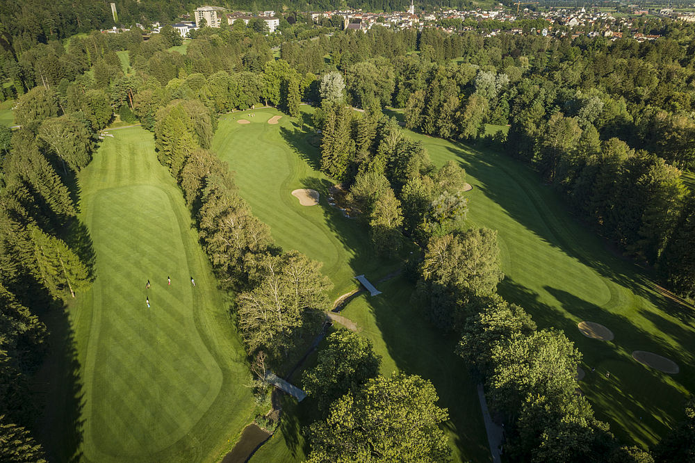 Luftaufnahme eines üppigen, von dichten Bäumen umgebenen Golfplatzes. Die Fairways sind sauber gestreift und bilden eine ruhige, gut gepflegte Landschaft.